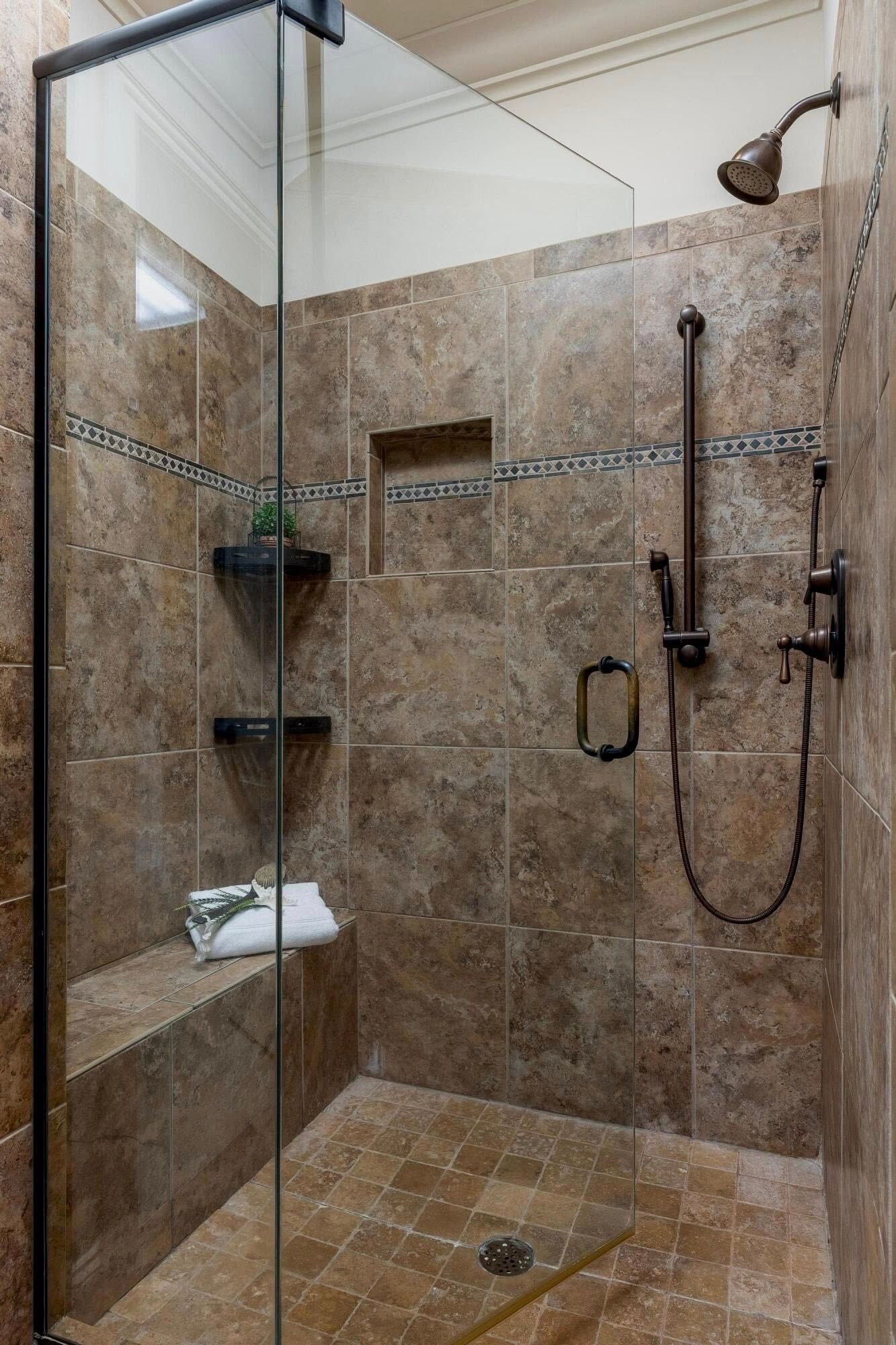 Glass-enclosed tiled shower with built-in corner shelves, grab bars, and a rainfall showerhead