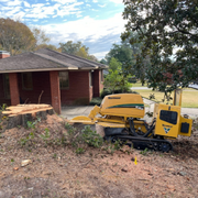Brick house with a yellow wood chipper in a yard covered with branches and debris