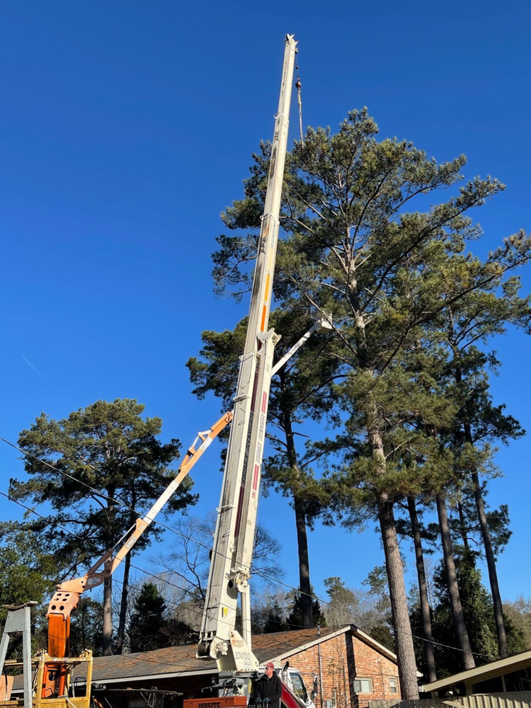 Crane lifting a tall utility pole beside a brick building under a clear blue sky