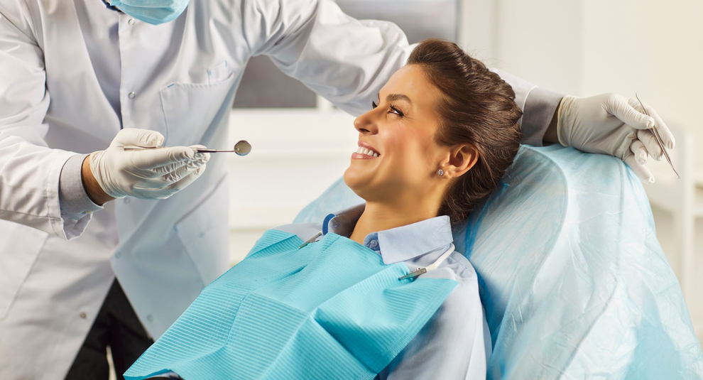Dentist in teal mask examining a patient in a dental chair, with assistant nearby in a bright clinic Dentist in teal mask examining a patient in a dental chair, with assistant nearby in a bright clinic