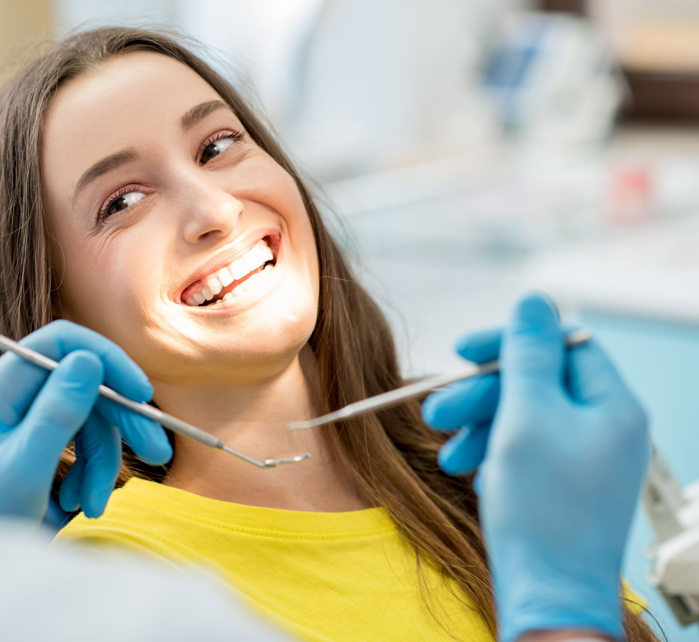 Dentist examining a smiling patient with blue-gloved hands in a dental chair