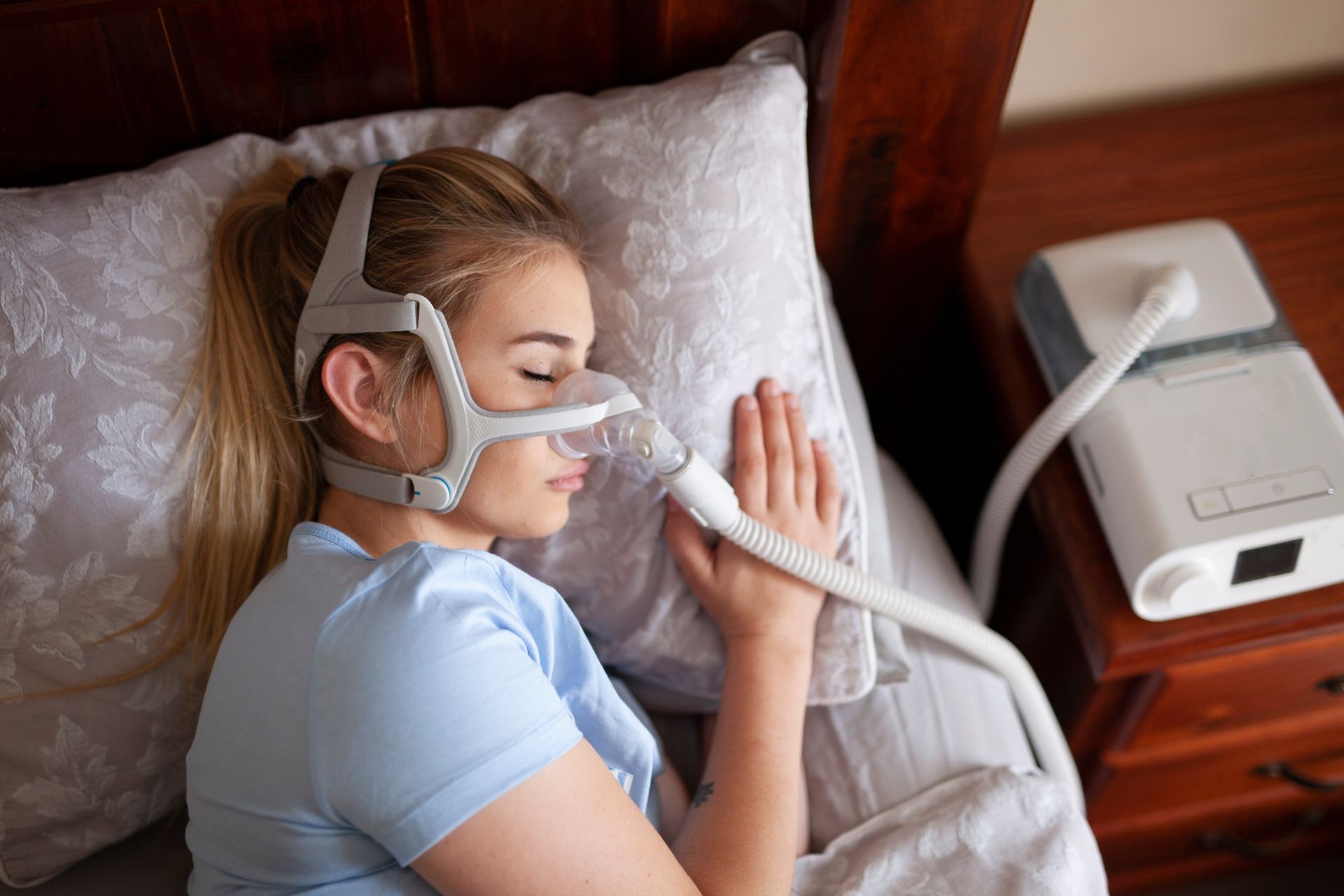 Person using a CPAP mask while lying in bed beside a bedside machine.