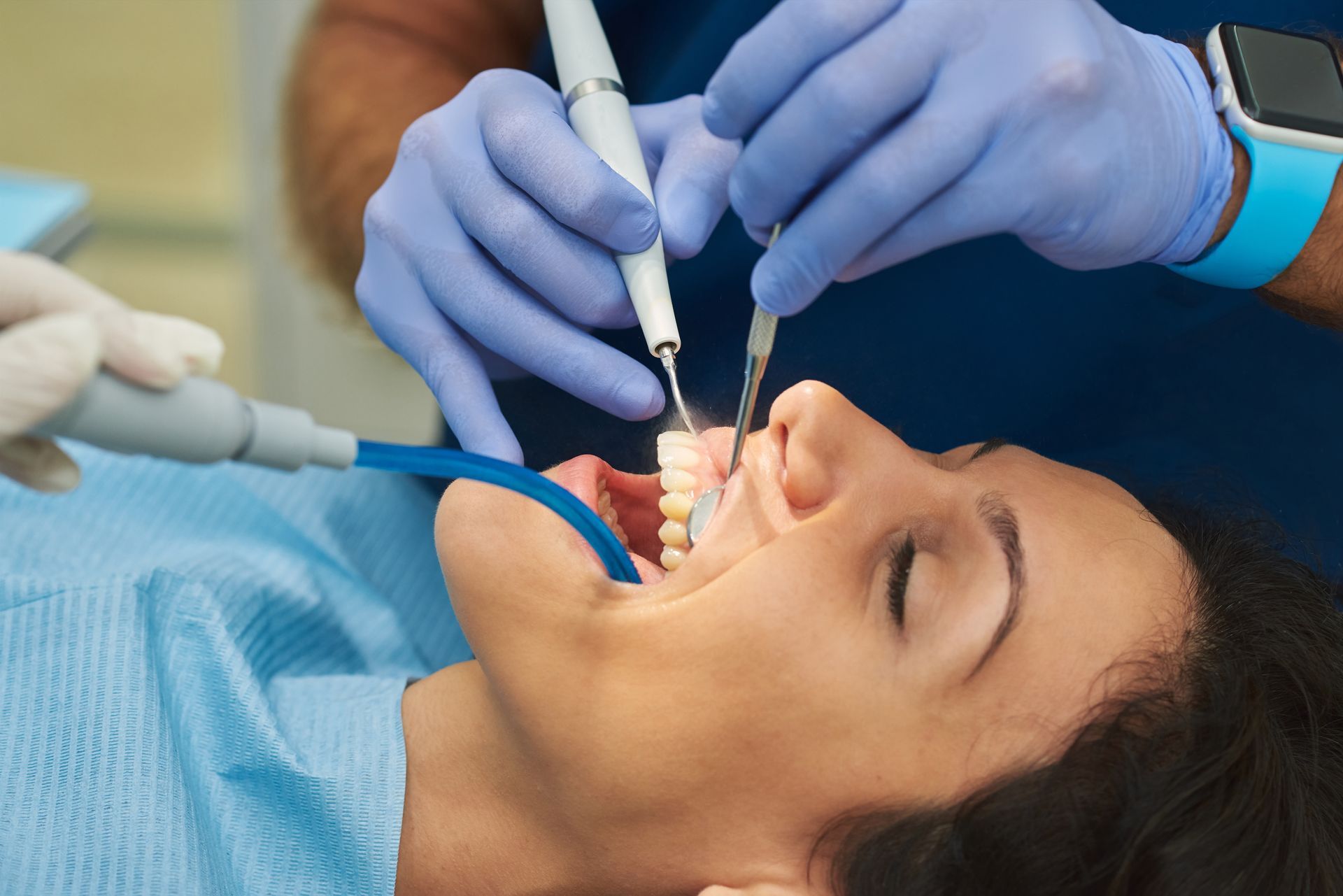 Dentist working on a patient in a dental chair, using tools near her open mouth.