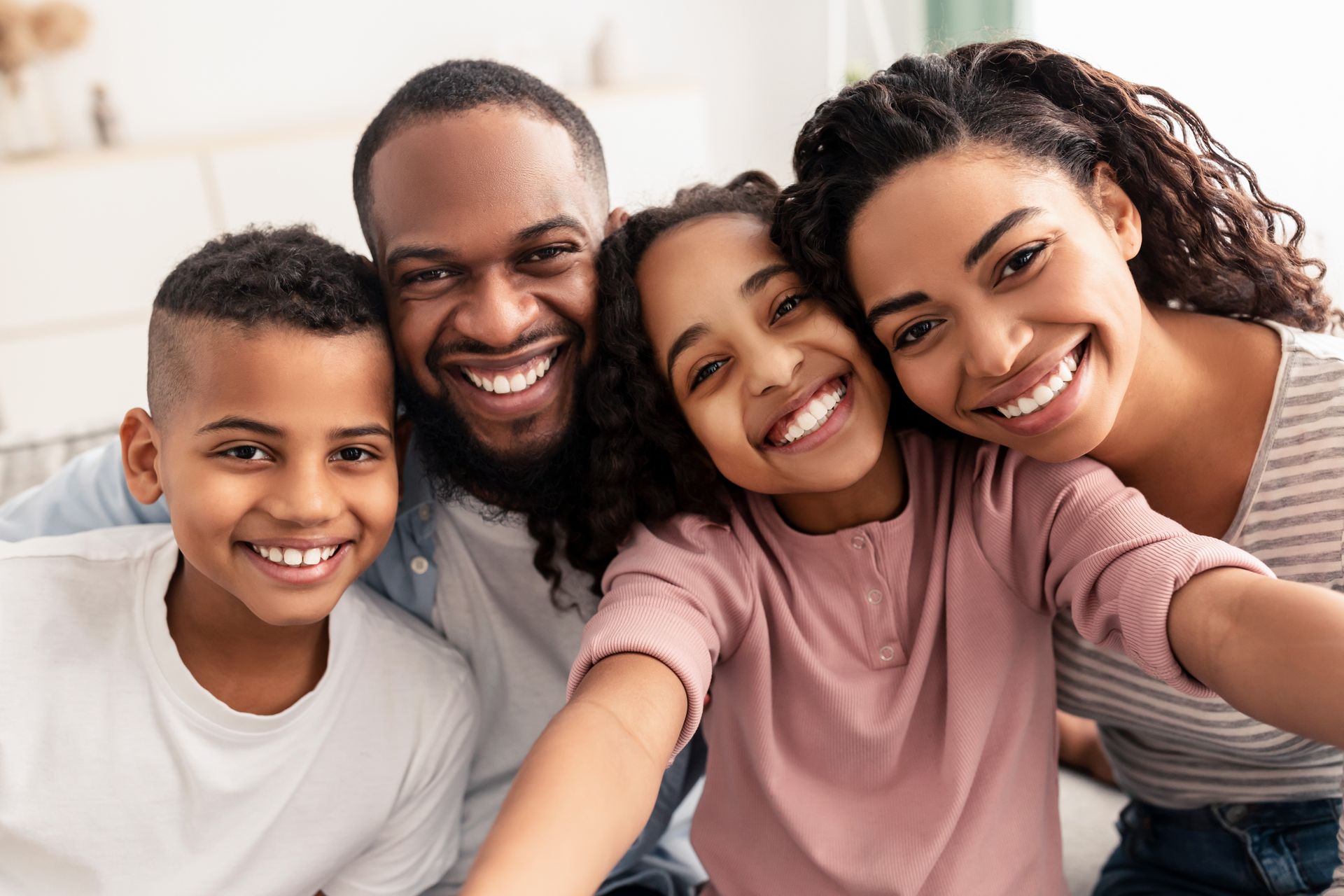 Four smiling people taking a selfie together on a couch in a bright living room