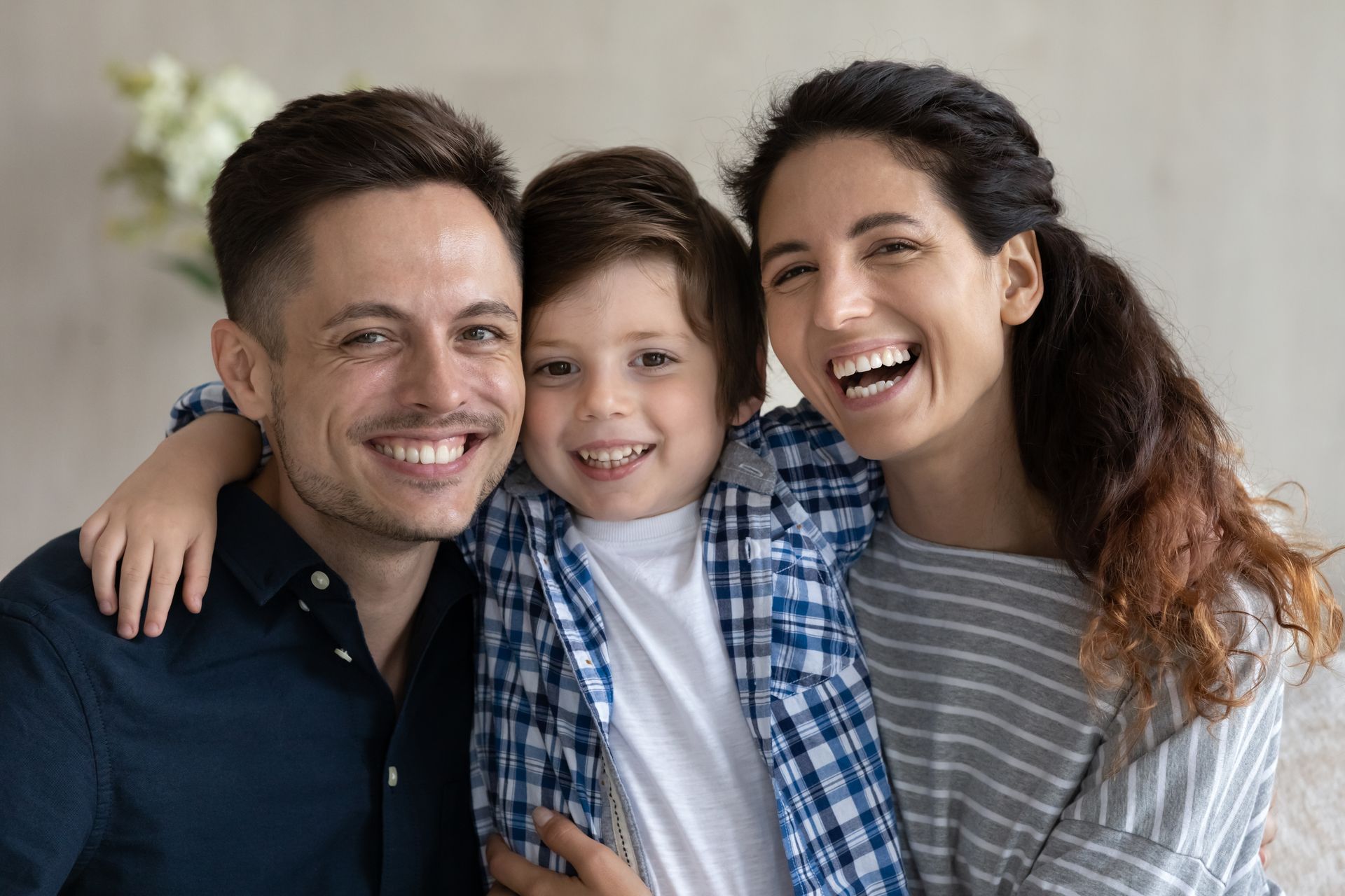 Three smiling people sitting close together indoors, with arms around each other, wearing casual clothes. Three smiling people sitting close together indoors, with arms around each other, wearing casual clothes.