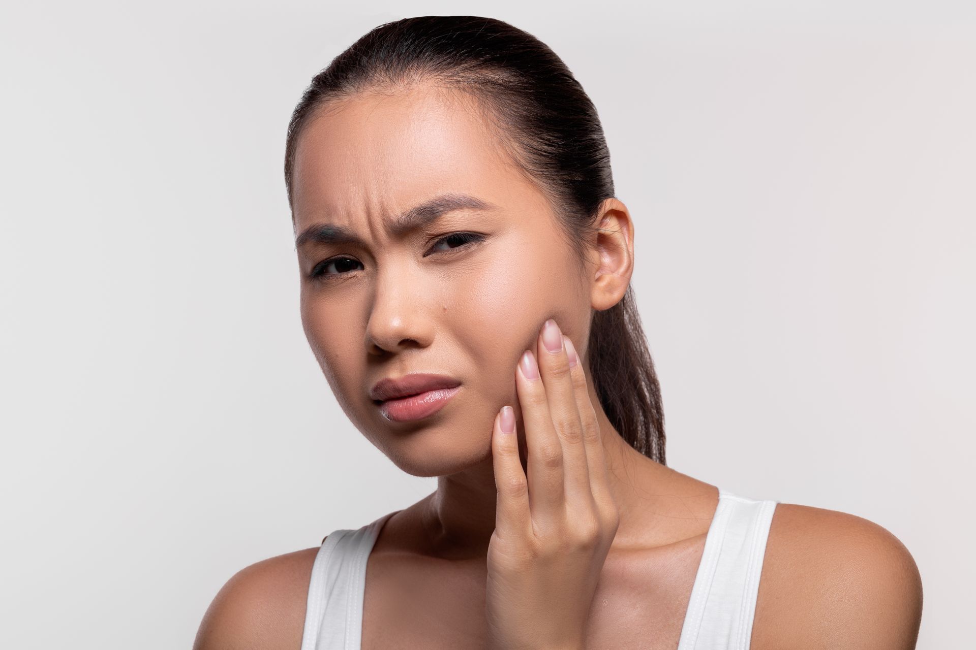 Woman touching her cheek with a pained expression, indicating tooth or jaw pain.