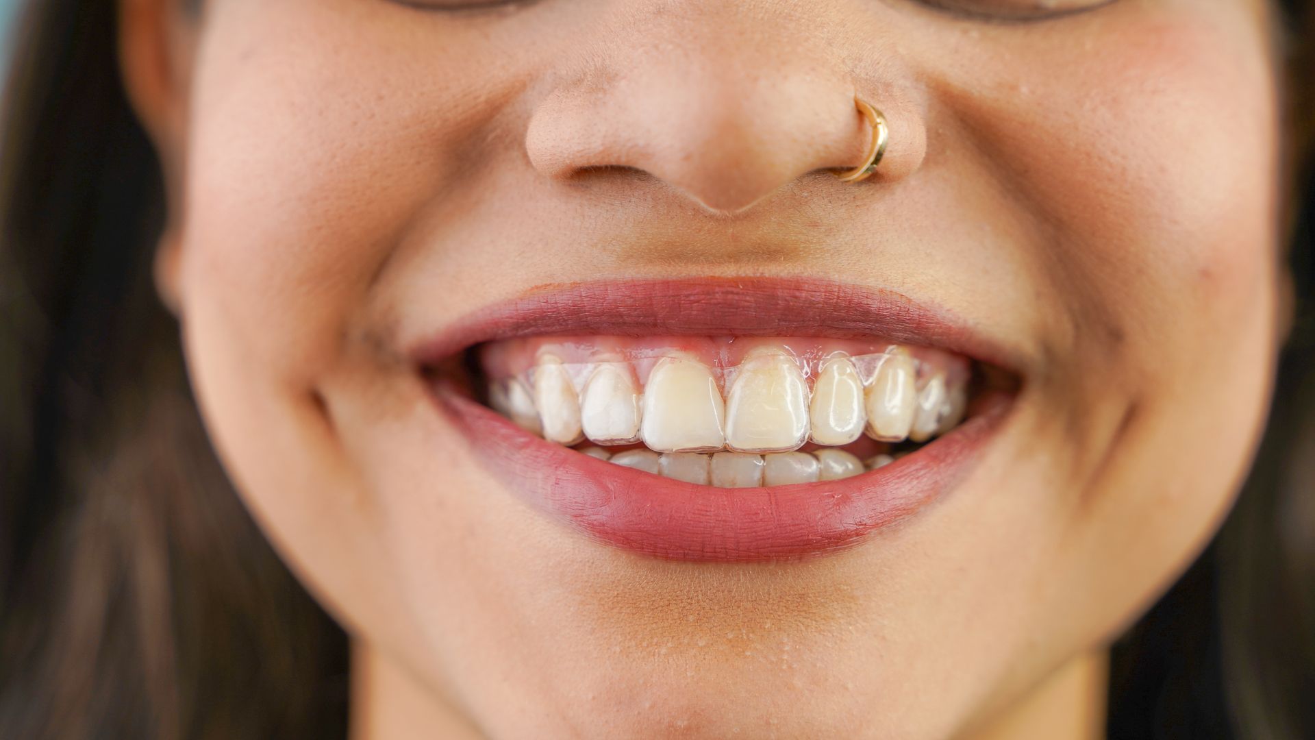 Close-up of a smiling mouth with bright teeth and a gold nose ring
