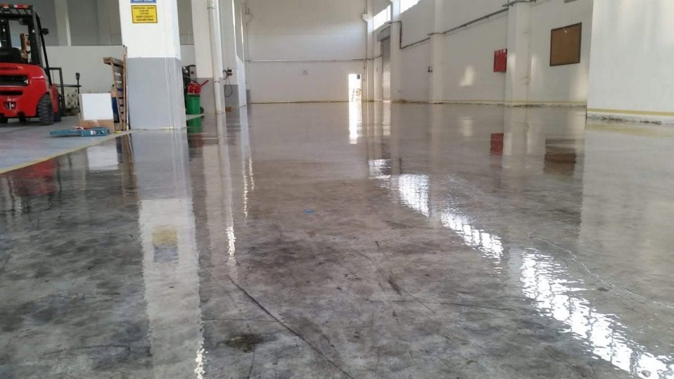 Polished concrete warehouse floor reflecting overhead lights in an empty industrial hall