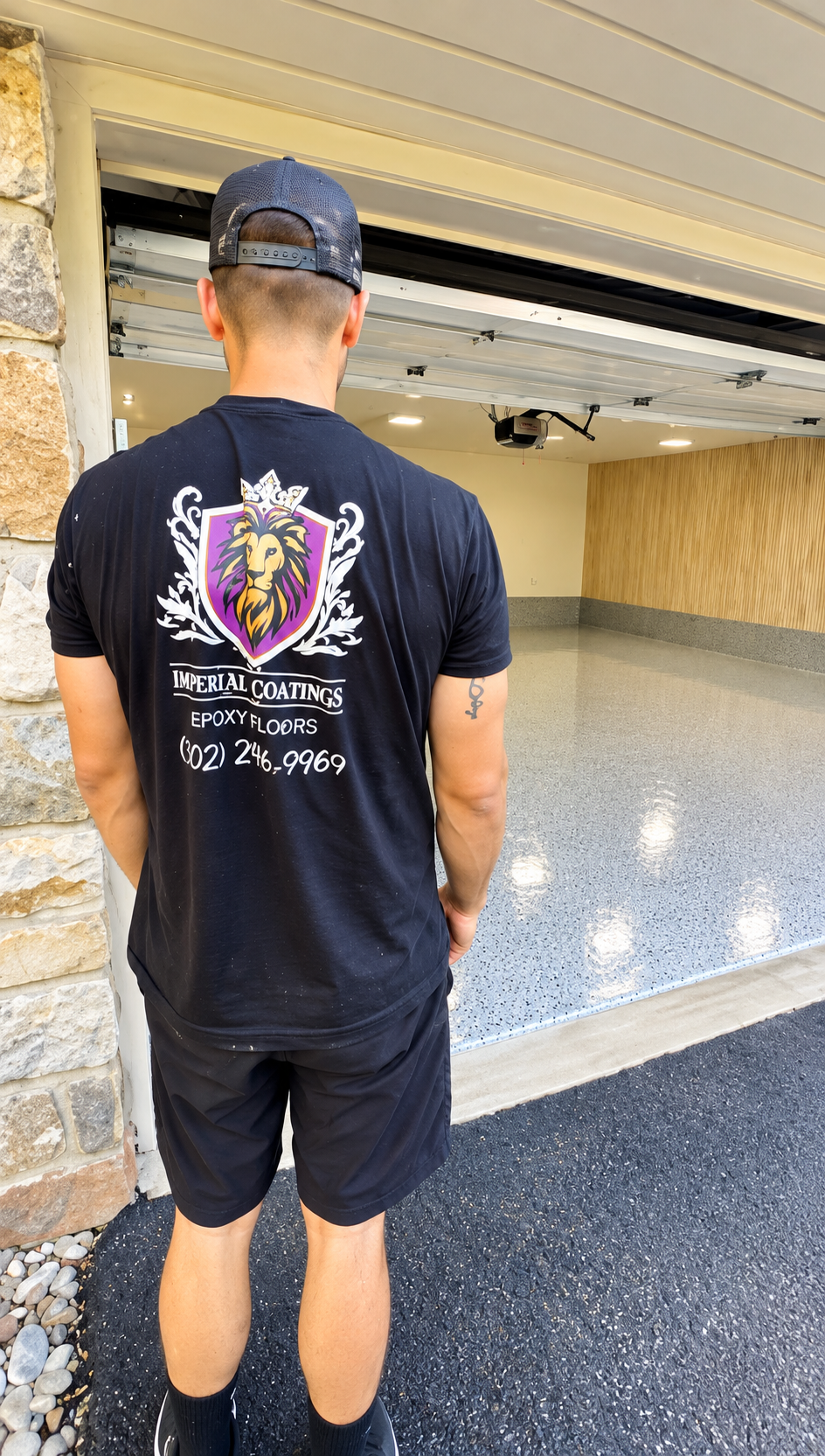 Man standing in a garage, seen from behind, wearing a black graphic T-shirt and shorts.