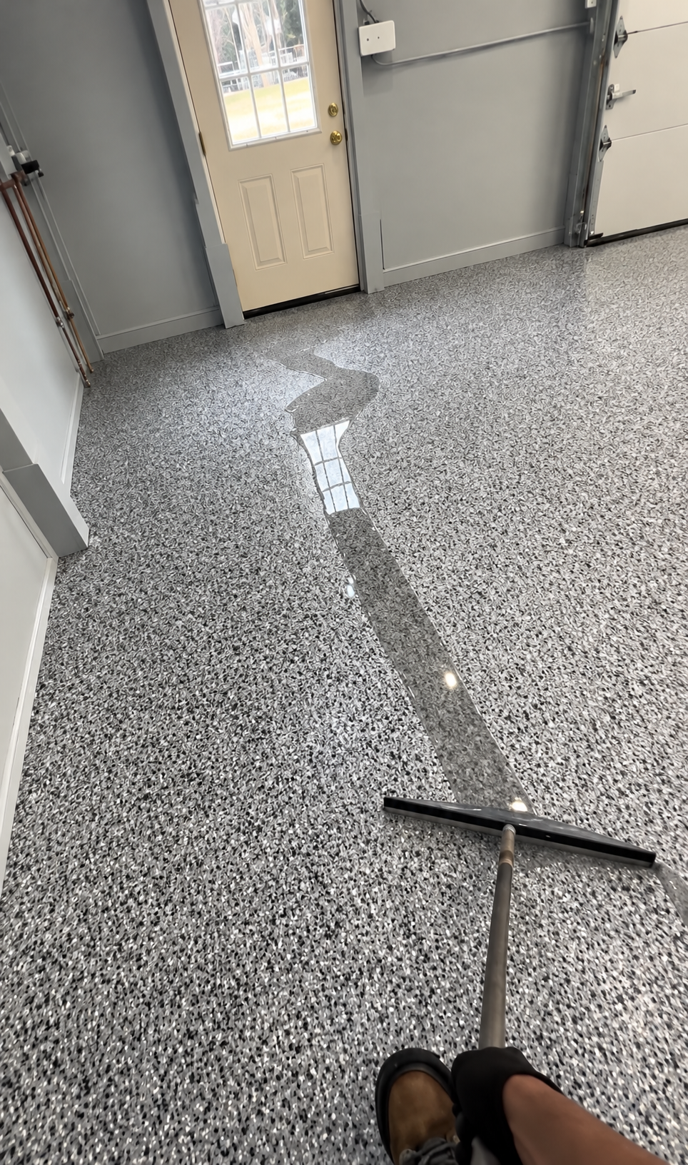 Person using a floor squeegee on a speckled hallway floor near doors