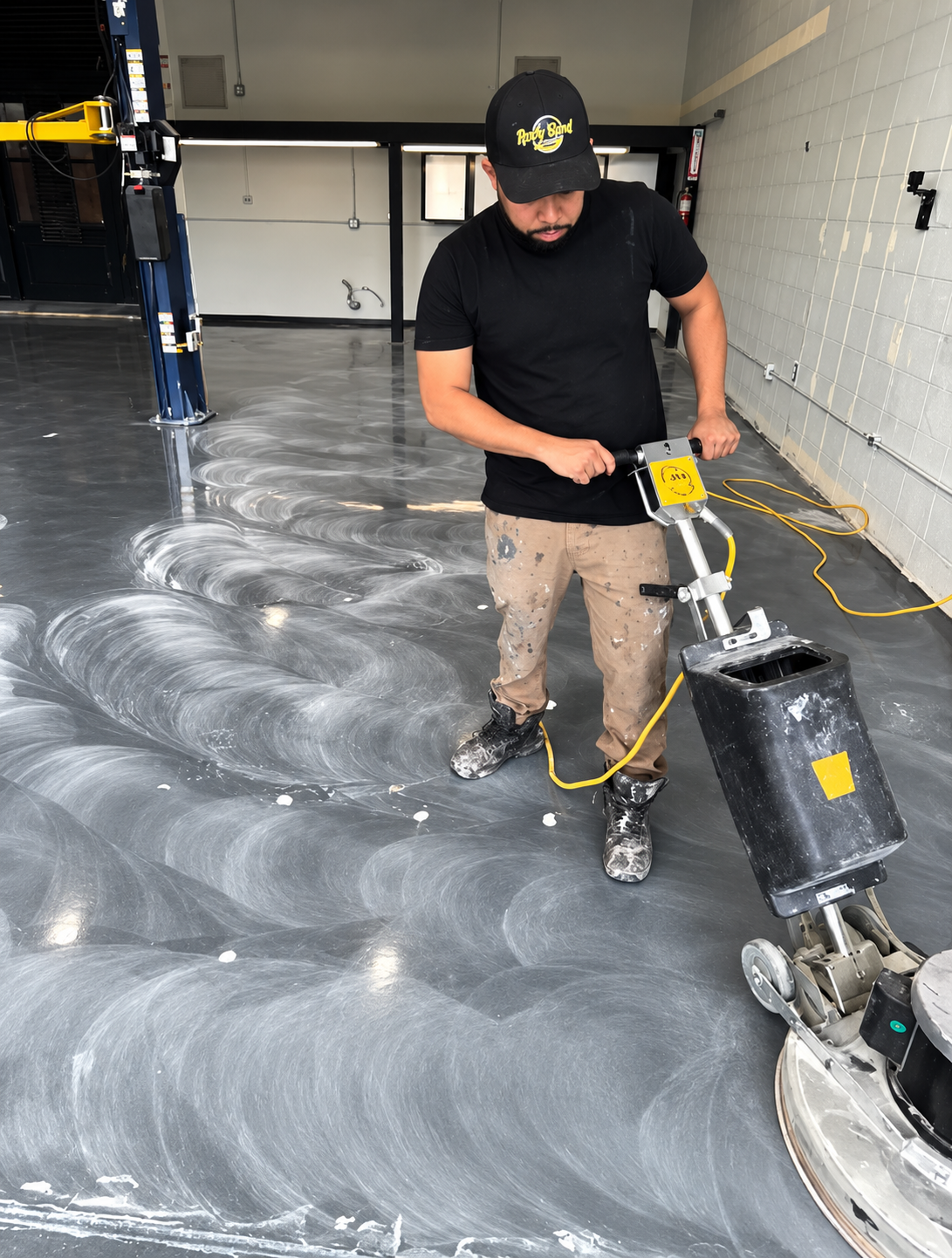 Worker polishing a concrete floor with a floor grinder in a garage.