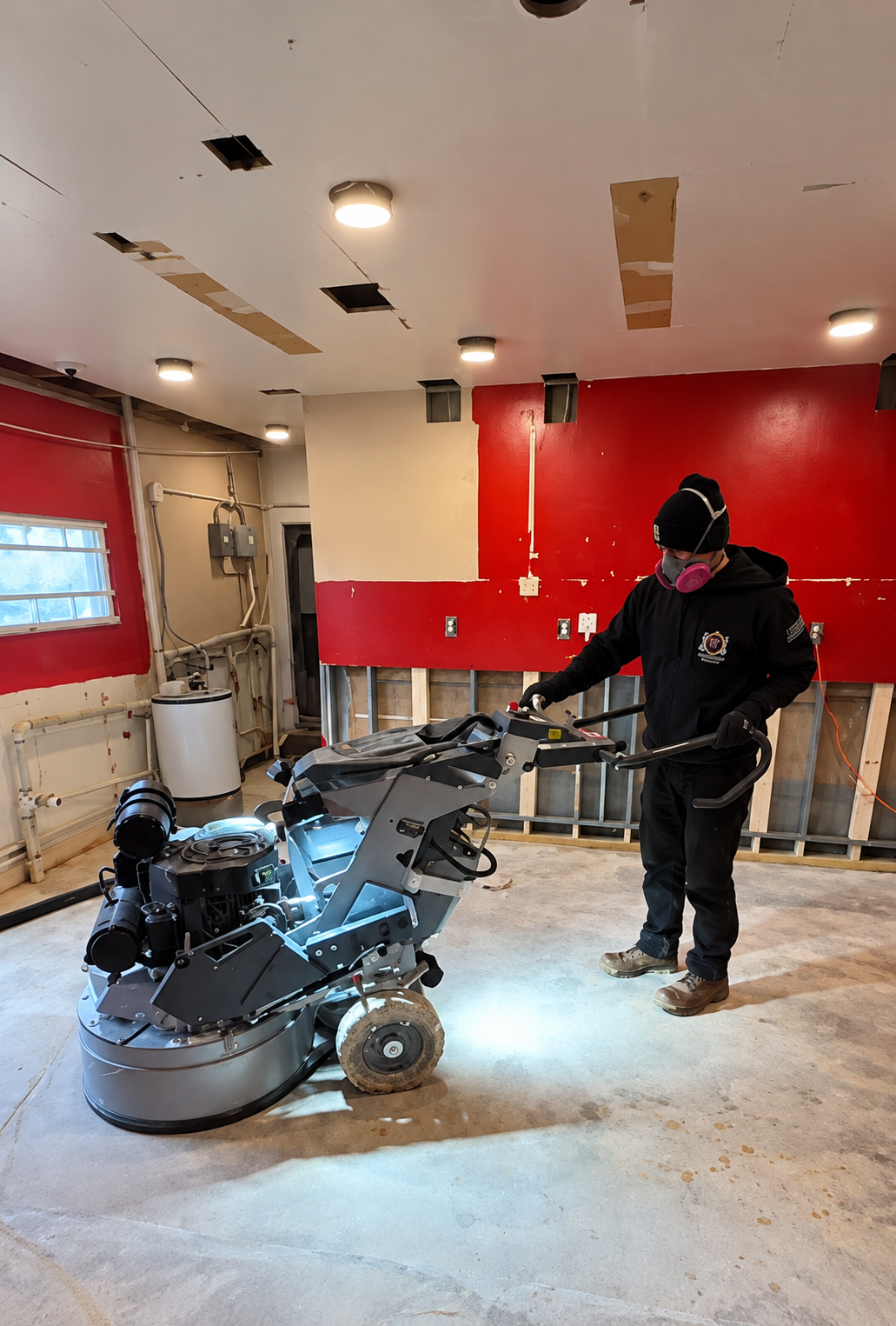 Person using a floor scrubber in a red-walled garage under renovation
