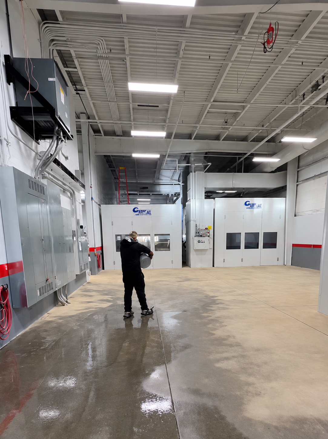 Warehouse interior with wet floor, overhead lights, and a person standing near large doors.