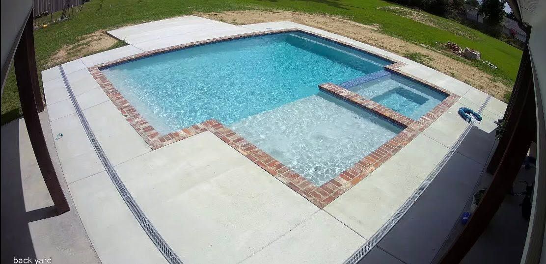 Backyard swimming pool with blue water, light concrete deck, and a narrow diving ledge