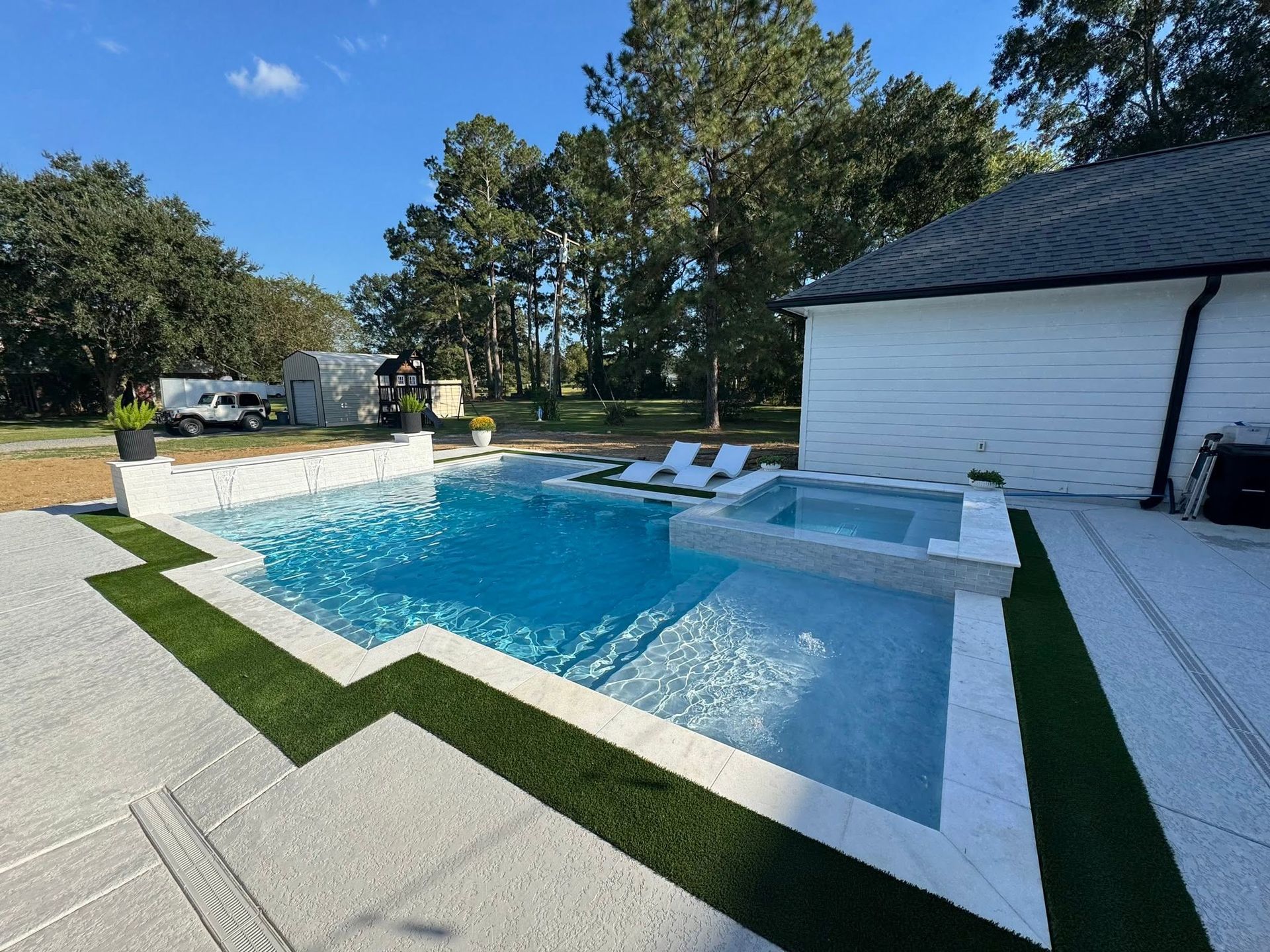 Backyard pool with white lounge chairs, blue water, and a white house beside a patio.
