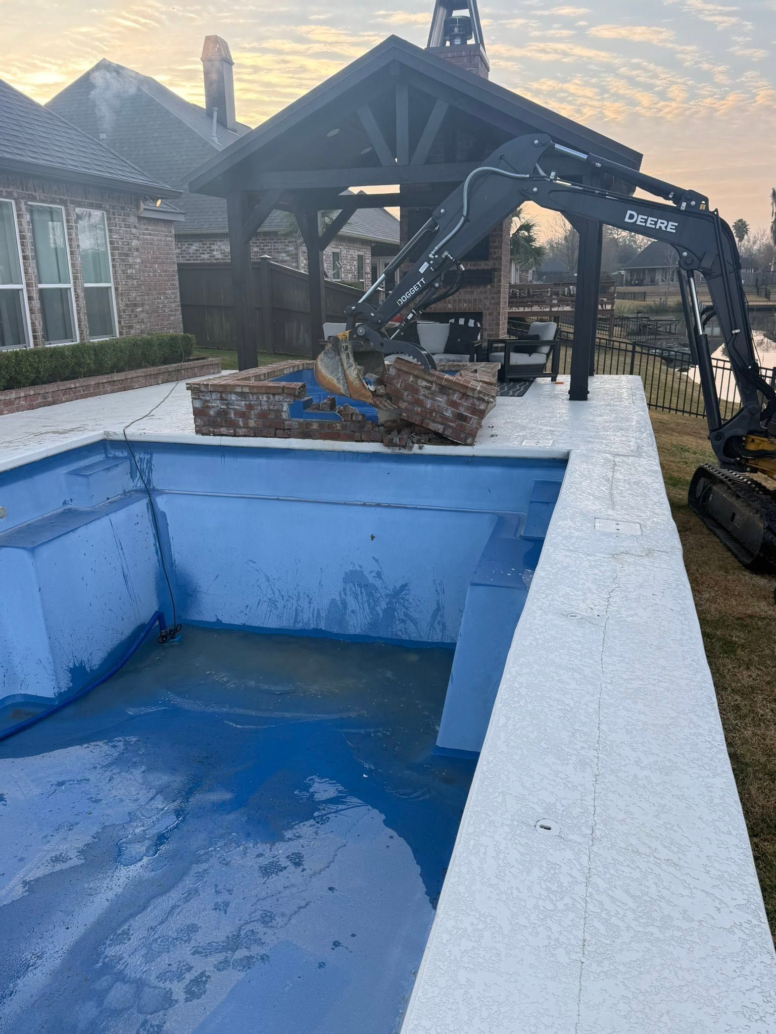 Empty blue swimming pool beside a patio and black pergola in a backyard at sunset