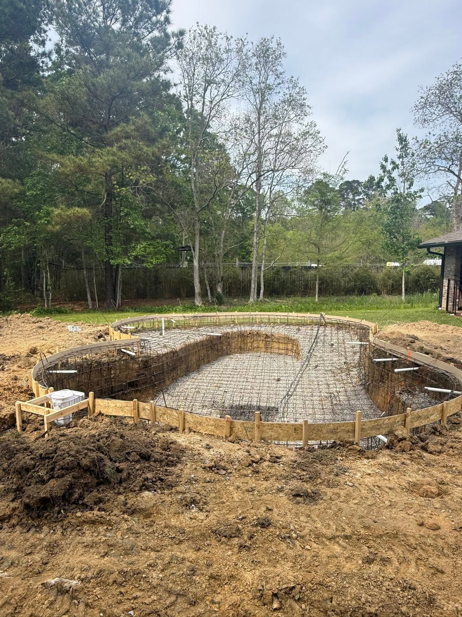 Circular concrete foundation in a dirt clearing with trees in the background, under construction.