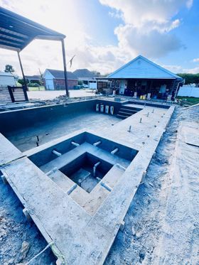 Outdoor concrete patio with a square fire pit, lounge chairs, and a blue-roofed pavilion by the water
