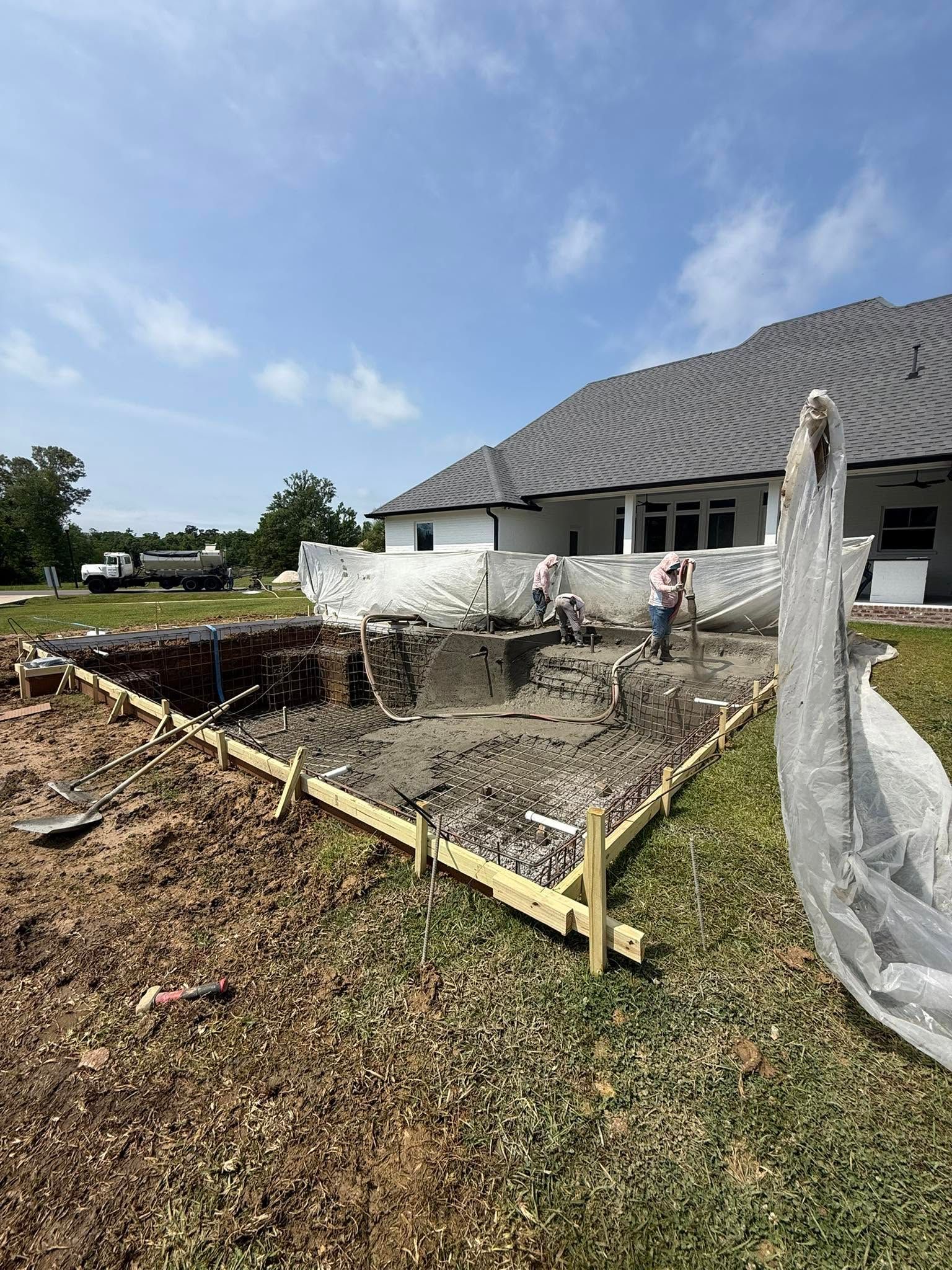 Backyard construction site with a newly framed foundation beside a white house under a blue sky