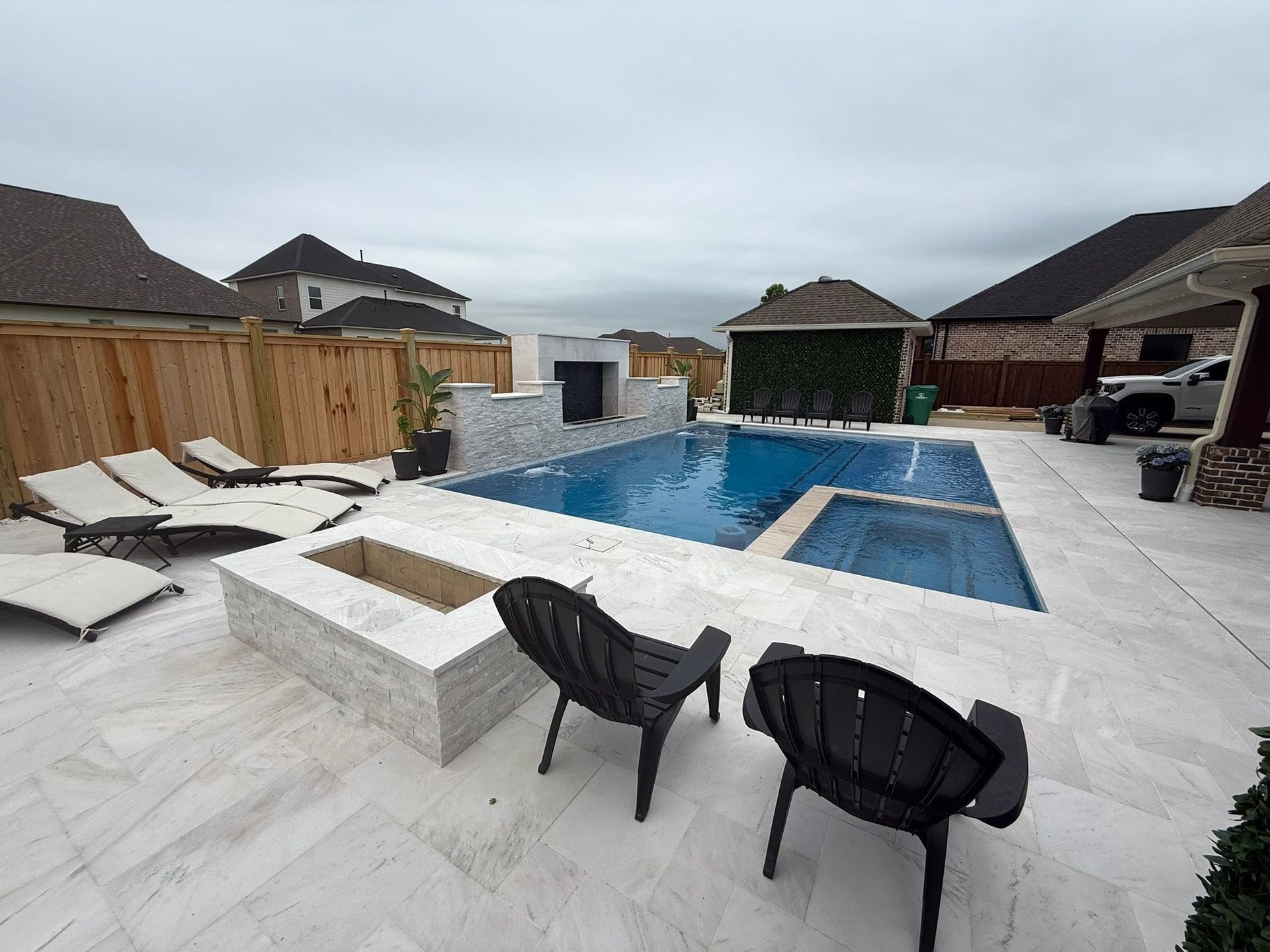 Backyard pool patio with white tile, lounge chairs, black chairs, and a covered gazebo