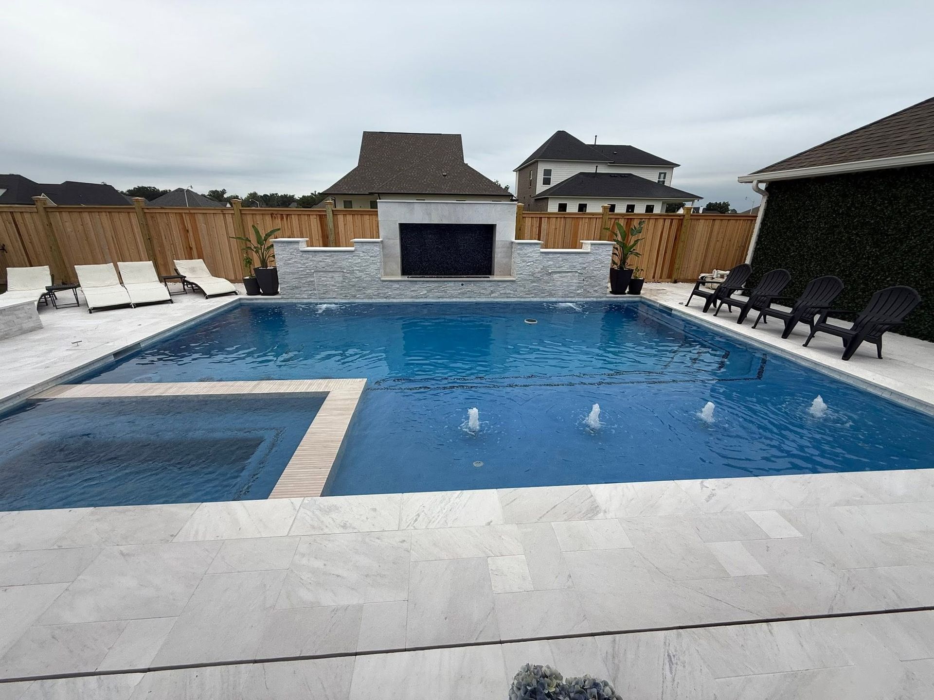 Backyard pool with blue water, white lounge chairs, a built-in firepit, and a stone patio.