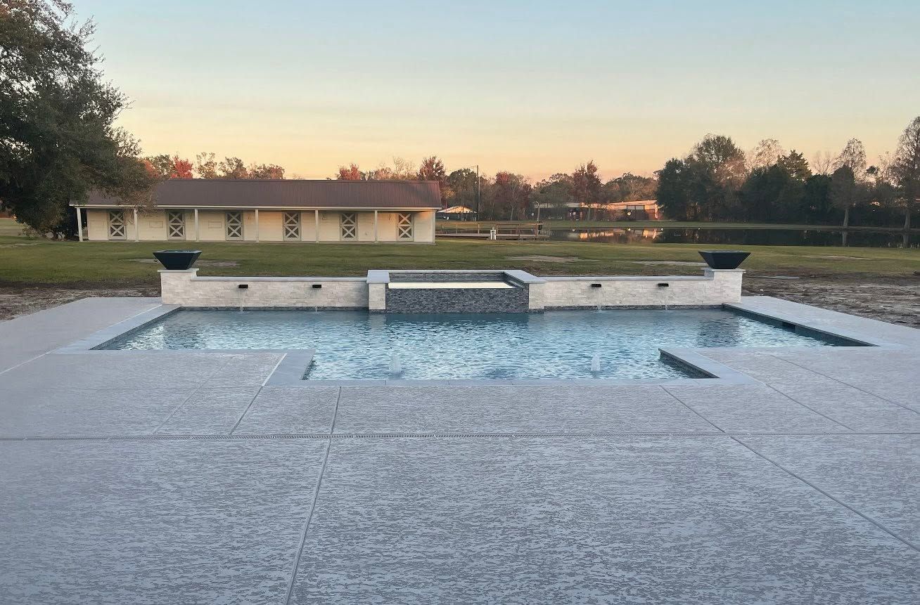 Stone pool with a central water feature at sunset, backed by a house and trees