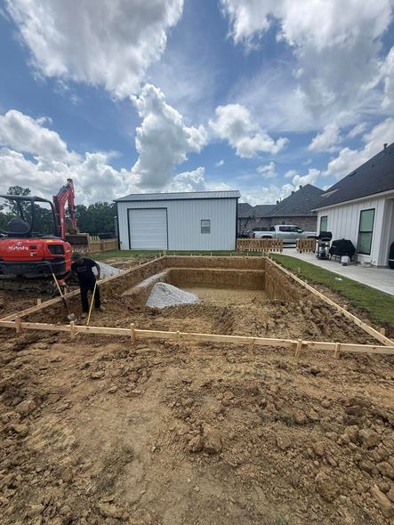 Construction site with excavated dirt, a red excavator, and portable buildings under a cloudy sky
