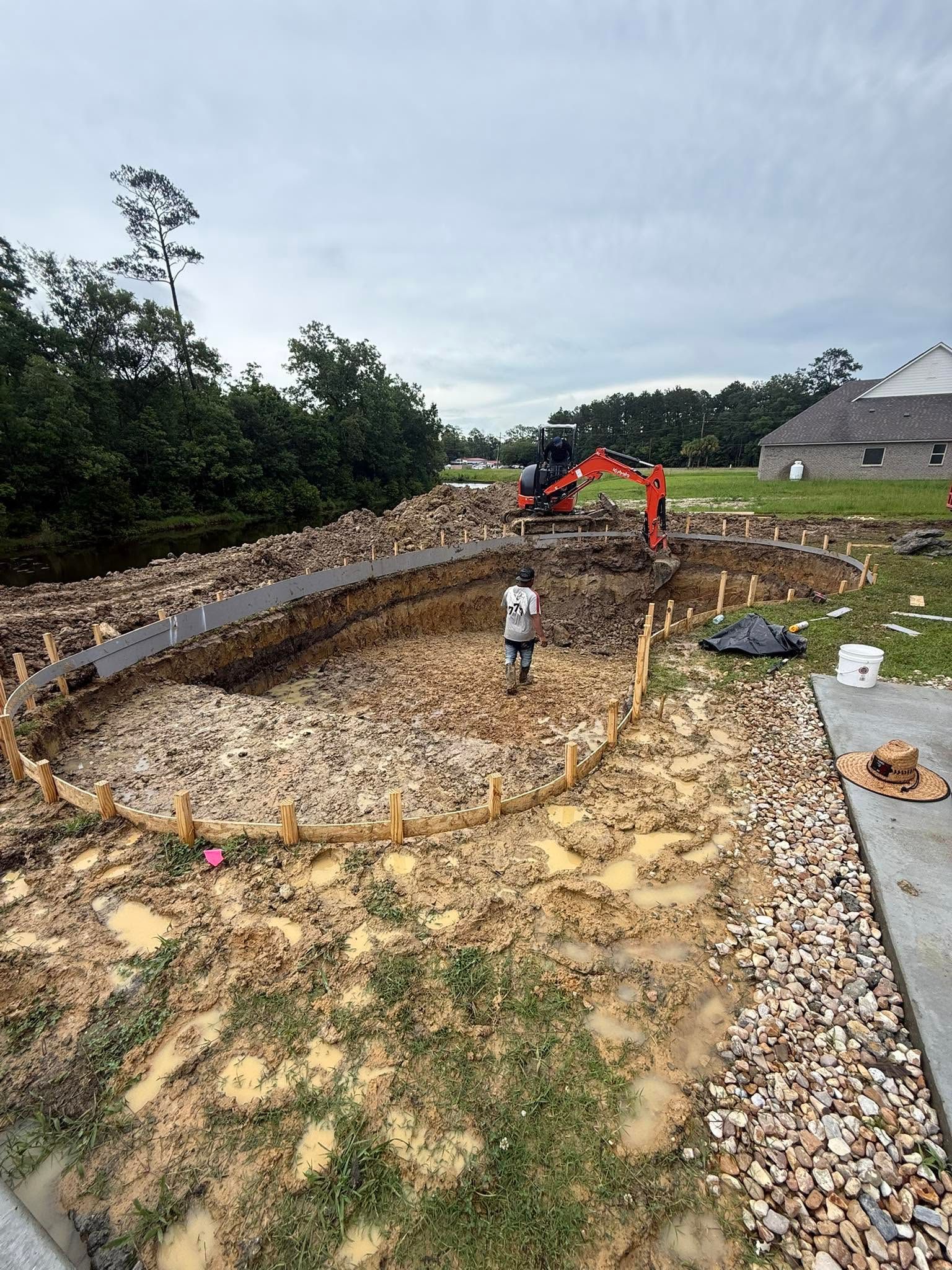 Construction site with excavator digging a curved foundation trench in a gravel-filled lot