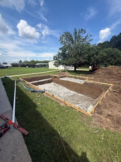 Backyard construction site with gravel trench, dirt, green lawn, and a tree under a blue sky