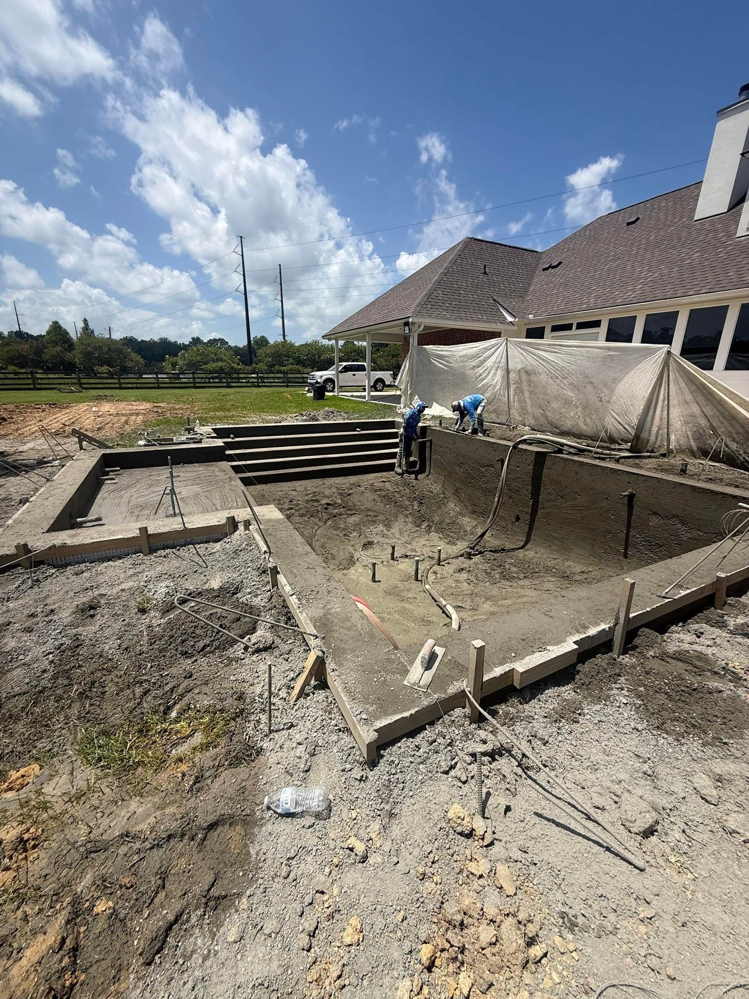Construction site with a large concrete foundation pit beside a house under a bright blue sky