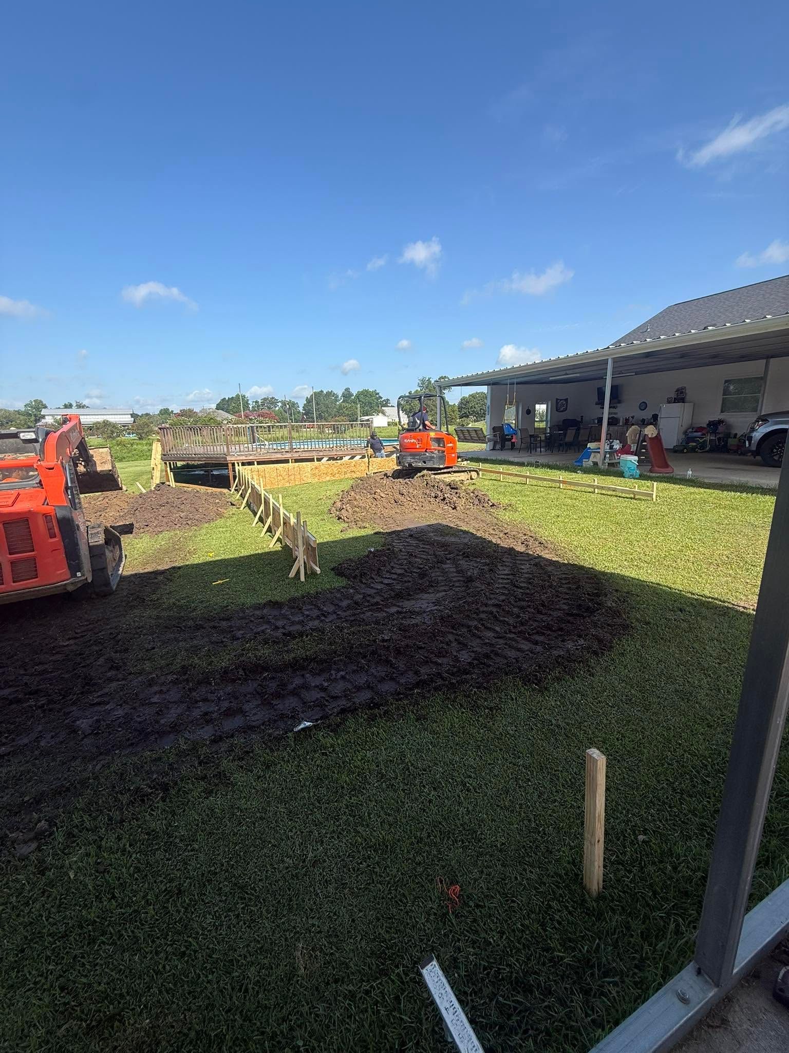 Backyard lawn under construction with orange equipment, soil piles, and a house under a blue sky
