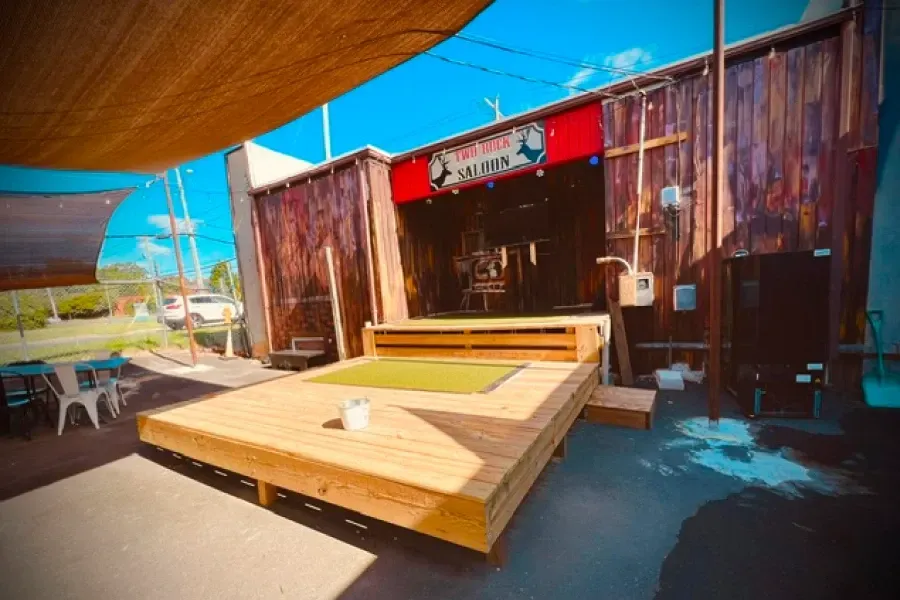 Wooden outdoor deck with benches and a shaded patio beside a rustic building under a bright blue sky
