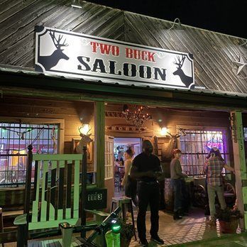 Two Buck Saloon bar entrance at night with neon lights and people gathered outside