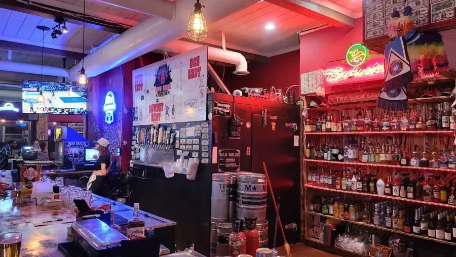 Cozy bar interior with red neon lights, shelves of liquor, and a long counter under warm hanging lamps