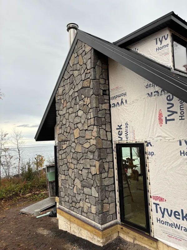 Stone-clad house exterior with black roof and unfinished doorway on a construction site