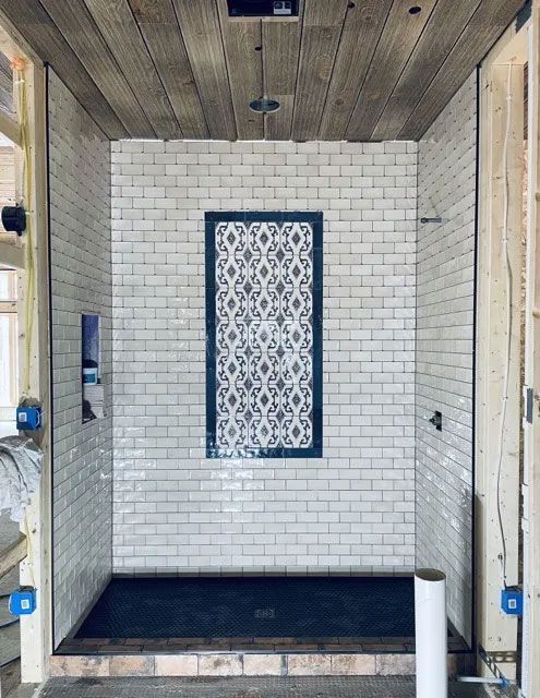 Tiled shower stall with black floor, white brick walls, and patterned tile accent panel.