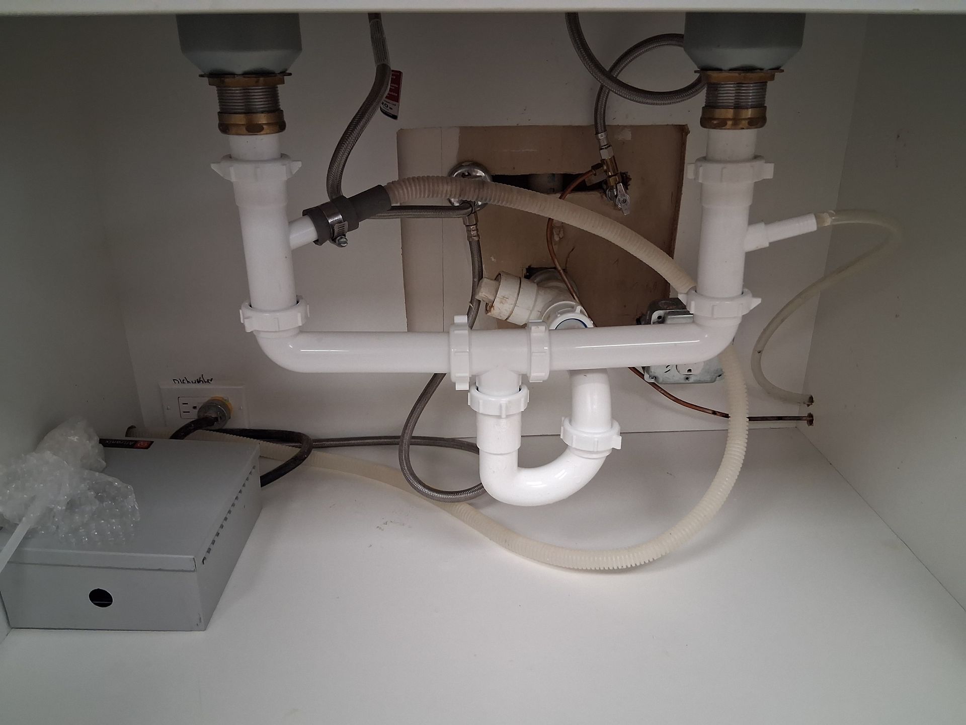 Under-sink plumbing with white PVC pipes and a gray garbage disposal in a cabinet