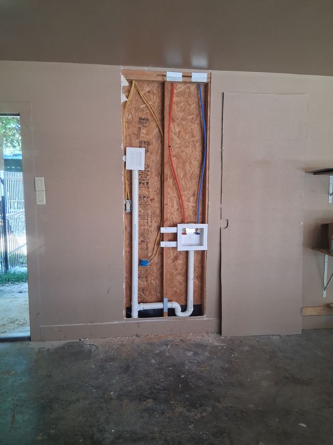Open wall with exposed wiring, insulation, and plumbing in a room under renovation.
