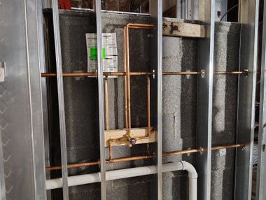 Exposed wall framing with insulation, copper pipes, and white PVC plumbing in a renovation area