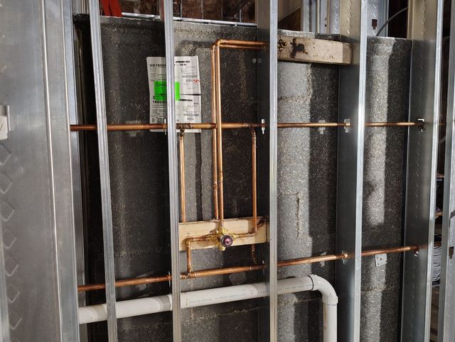 Exposed wall framing with insulation, copper pipes, and white PVC plumbing in a renovation area