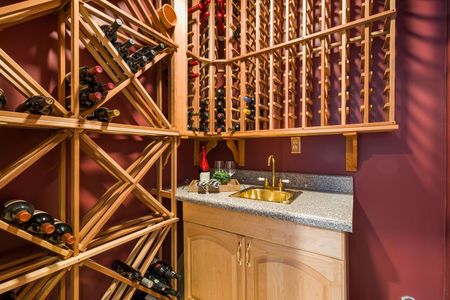 Wine cellar with wooden racks, bottles, and a small sink with granite countertop.