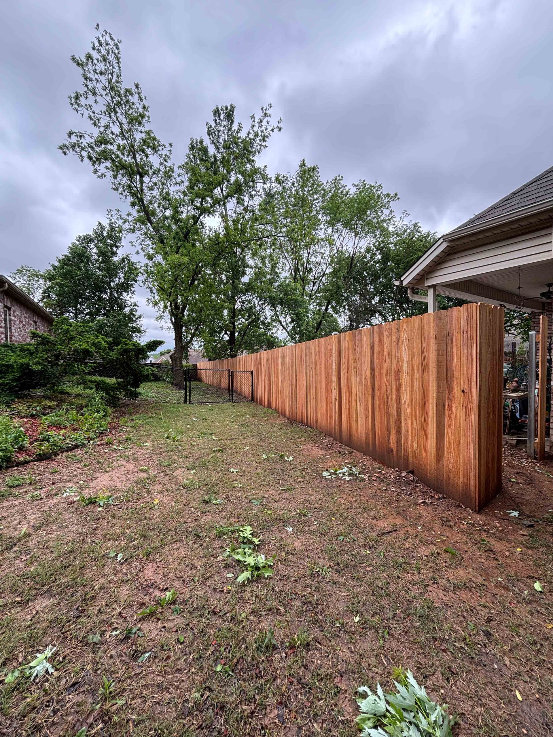 Backyard with a wooden privacy fence beside a house under a cloudy sky