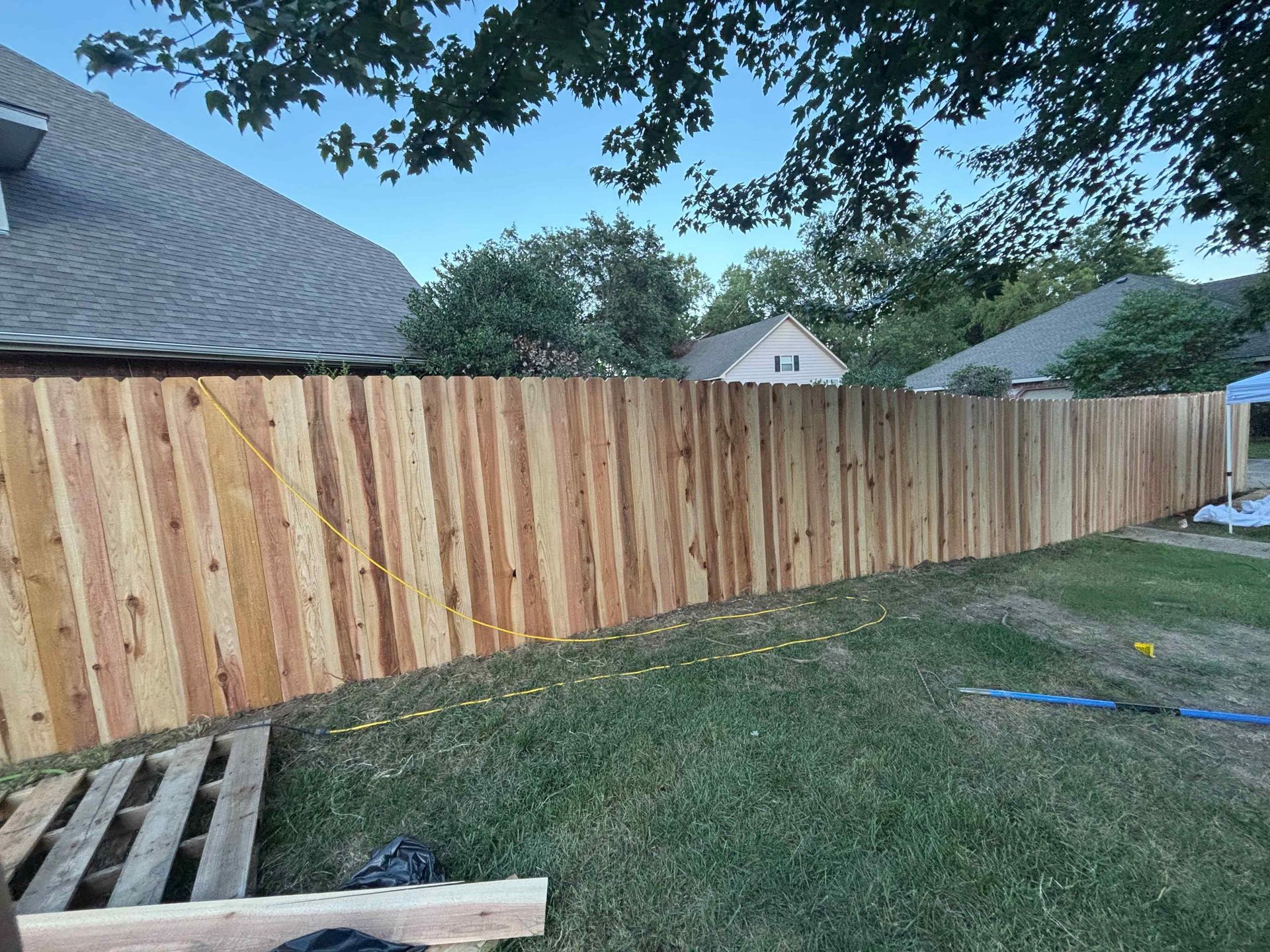Wooden privacy fence along a grassy backyard beside houses under a blue sky