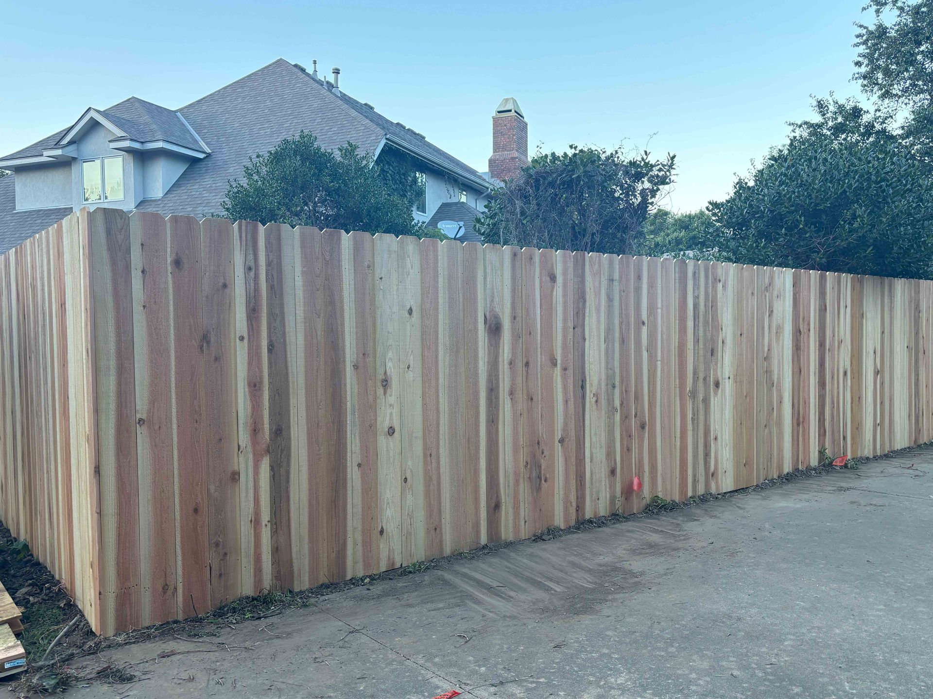 Tall wooden privacy fence along a driveway with a house and trees behind it