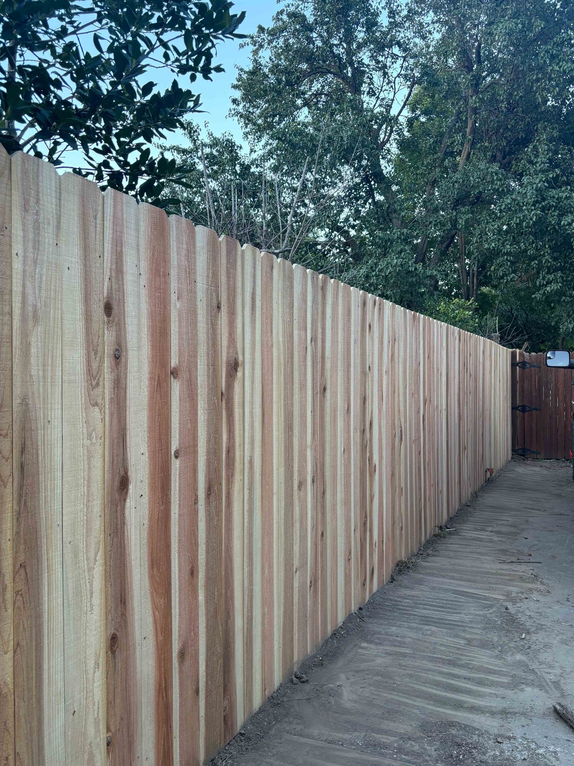 Long wooden fence beside a narrow dirt path, with trees overhead.