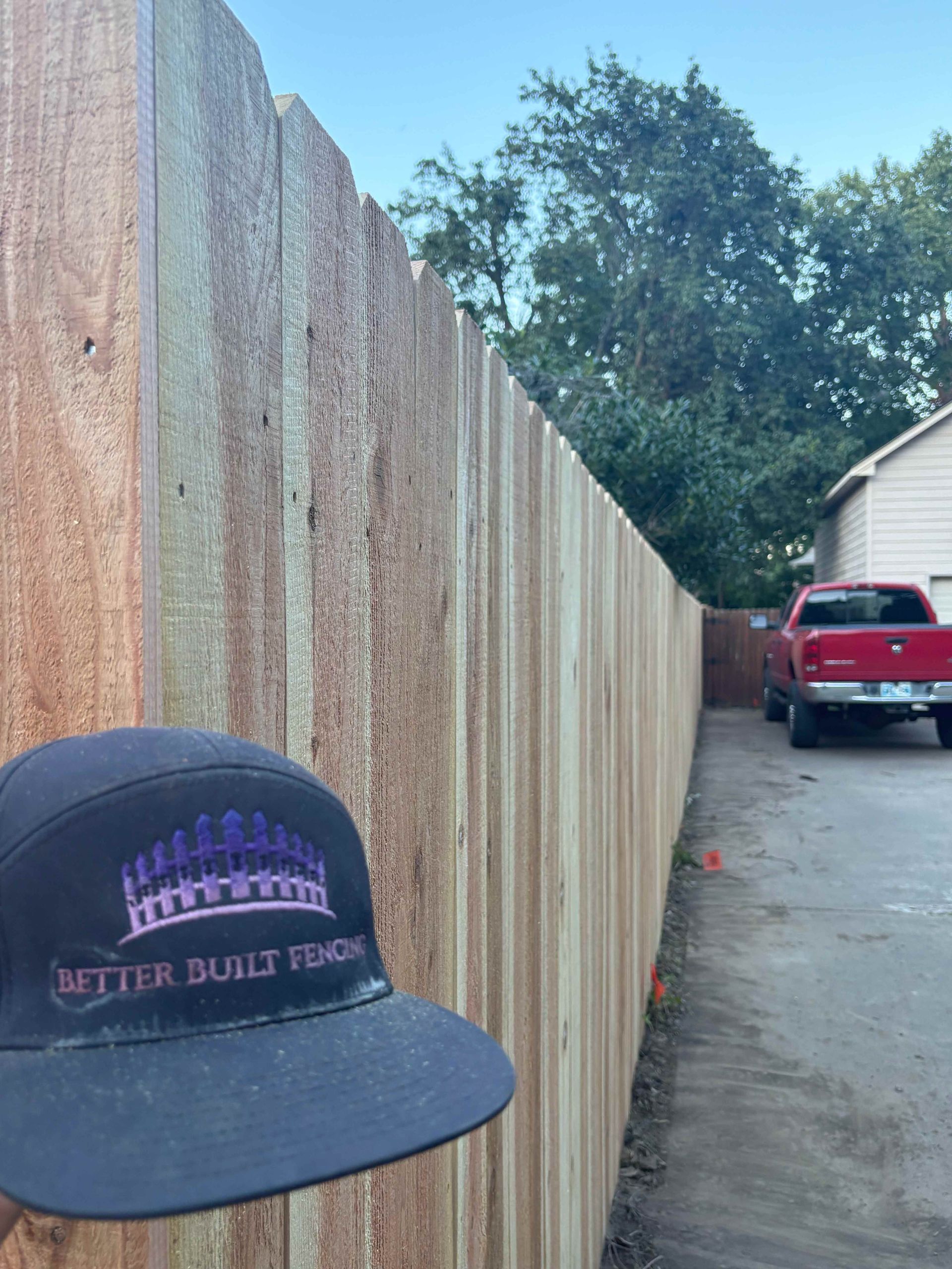 Fence-lined driveway with a red SUV and a black cap in the foreground