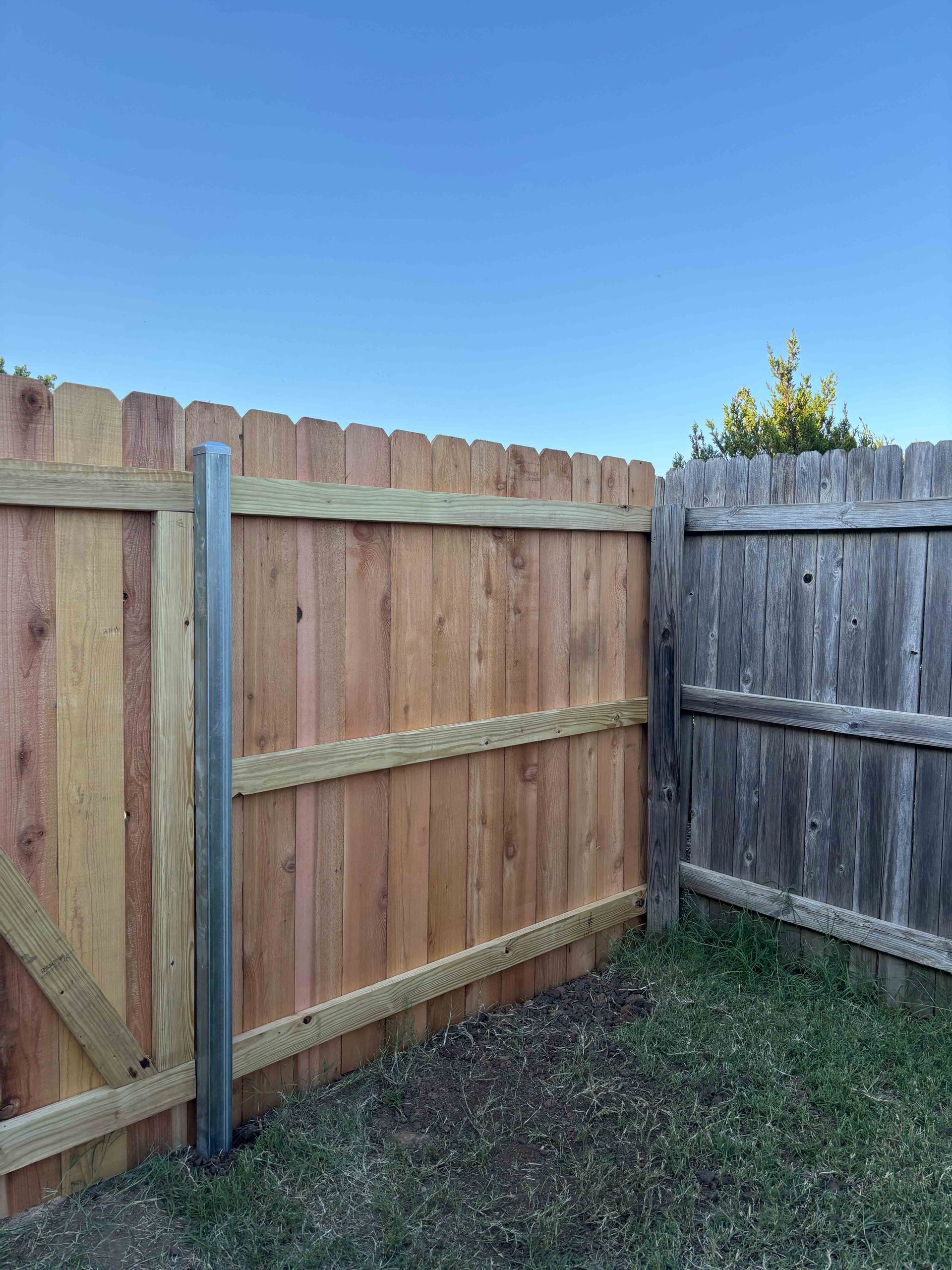 Wooden backyard fence corner with a blue post under a clear sky