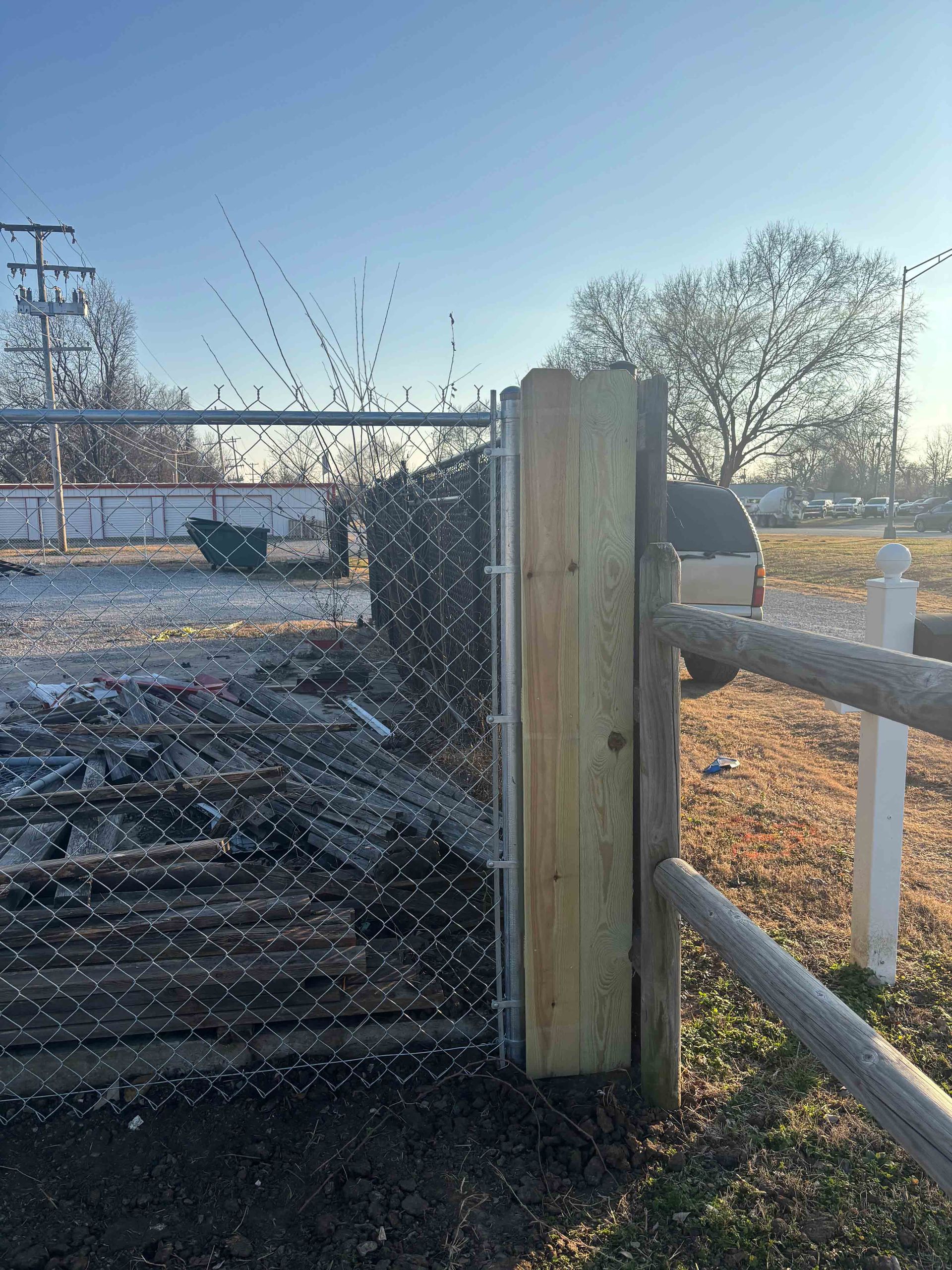 Chain-link gate with wooden posts and rails in a frosty yard at sunrise