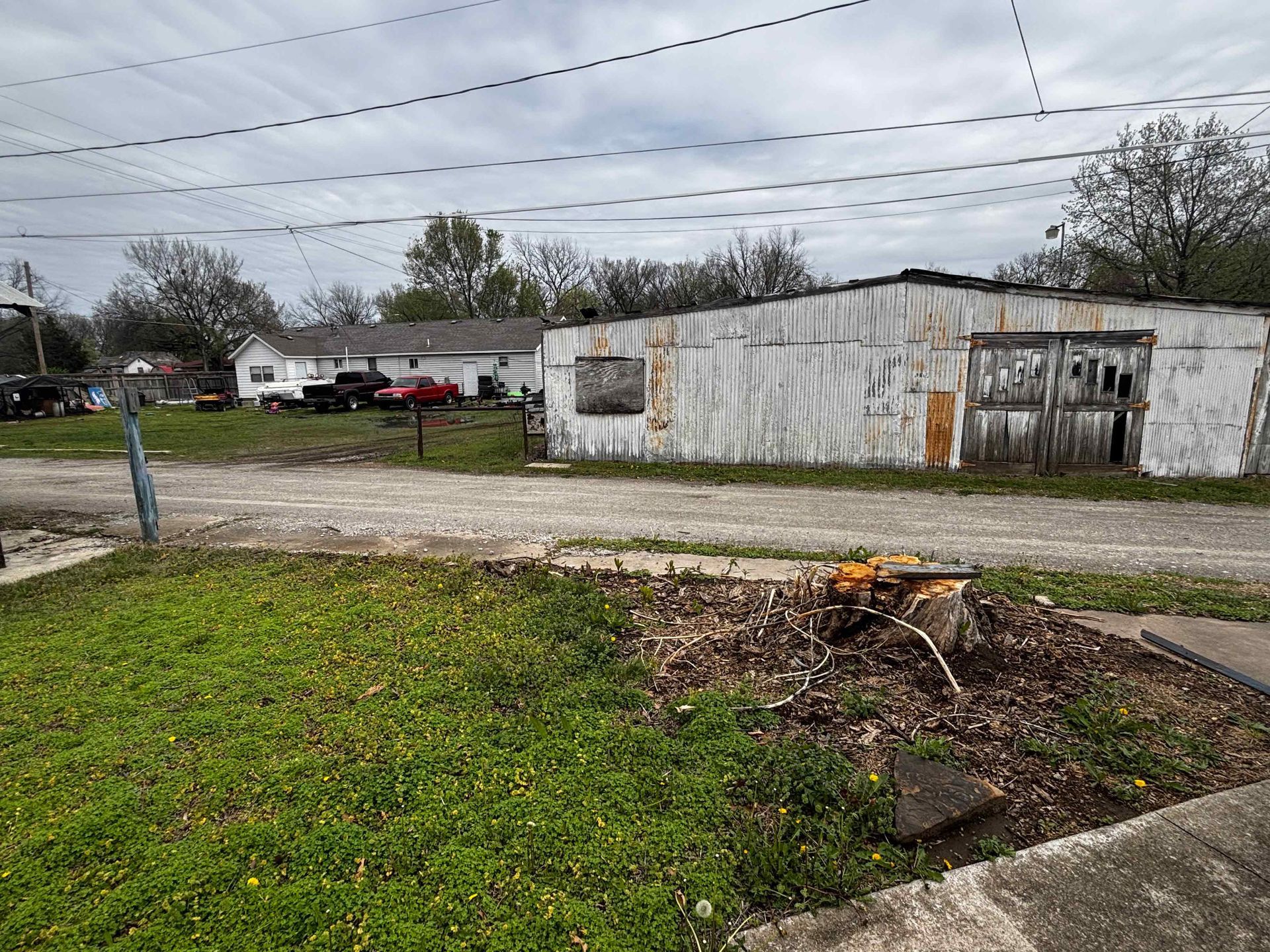 Rundown white building beside a road, with a grassy lot and cloudy sky.