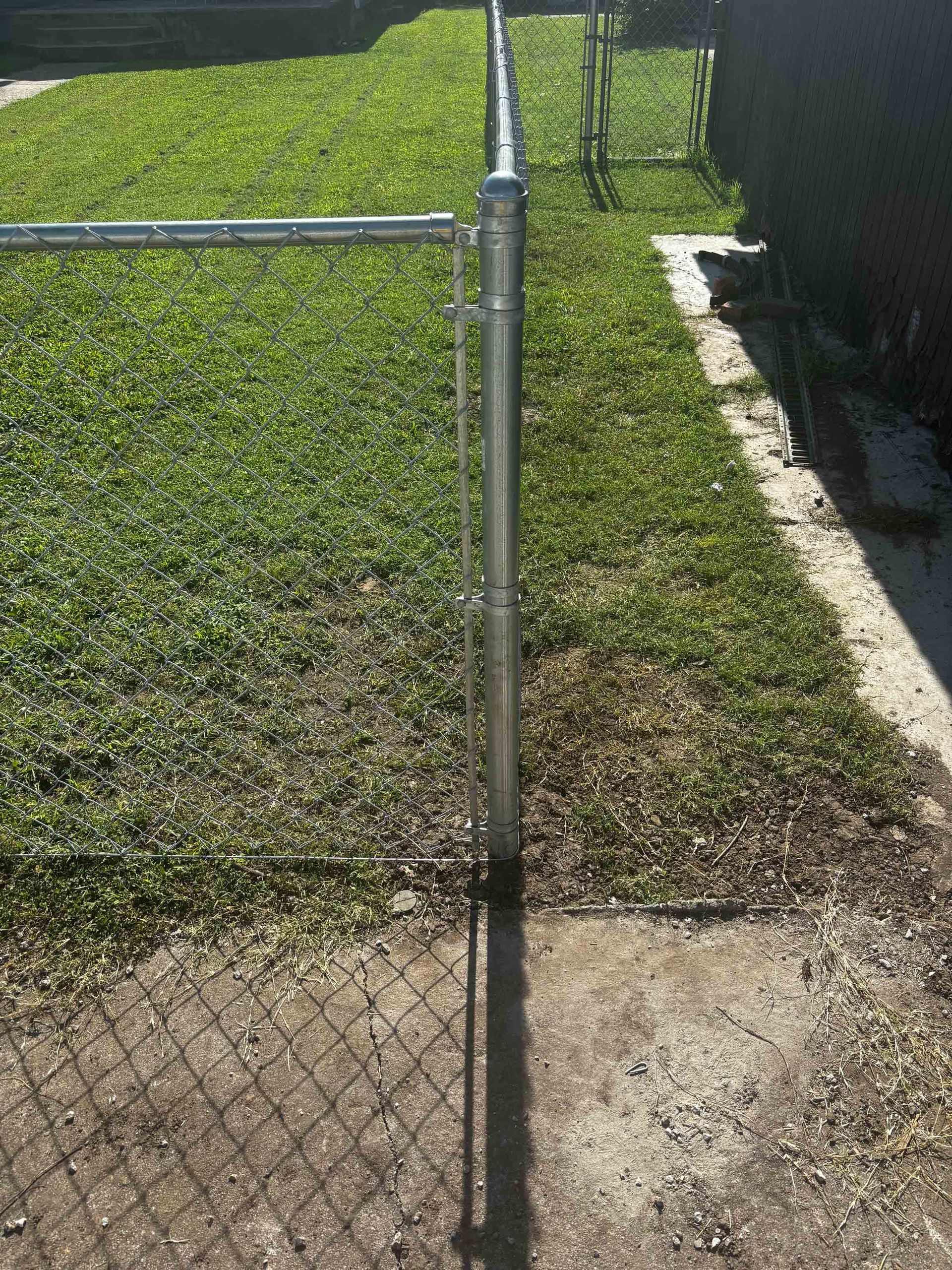 Chain-link fence in front of a grassy yard with a concrete path and black fence on the right.